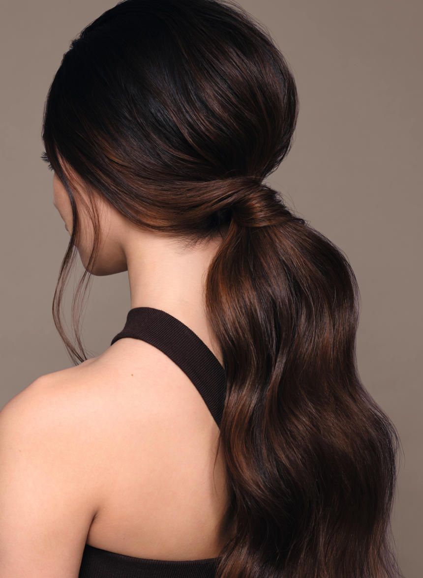 Gros plan d'une femme aux cheveux bruns attachés en queue de cheval. Les cheveux sont ondulés.