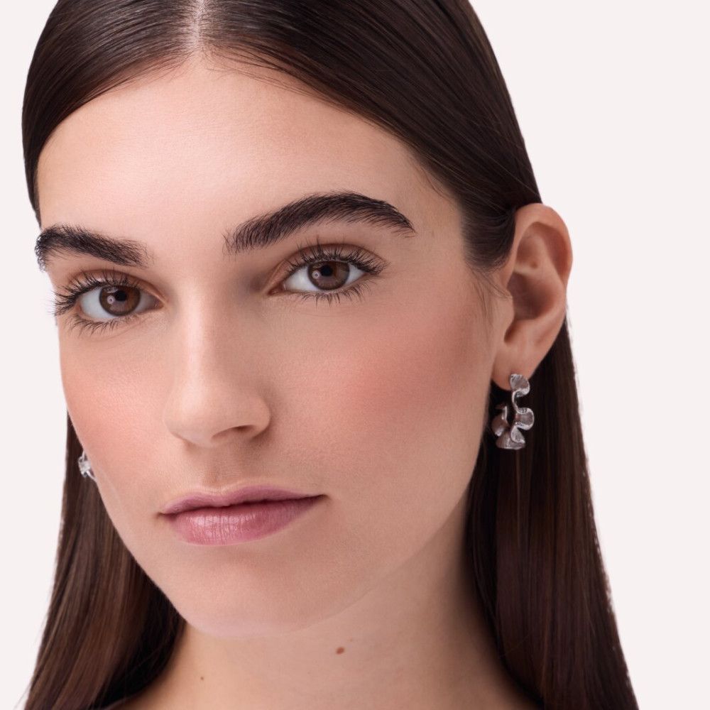 Portret van een vrouw met blush op de wangen. Ze draagt oorbellen. Lichte achtergrond.
