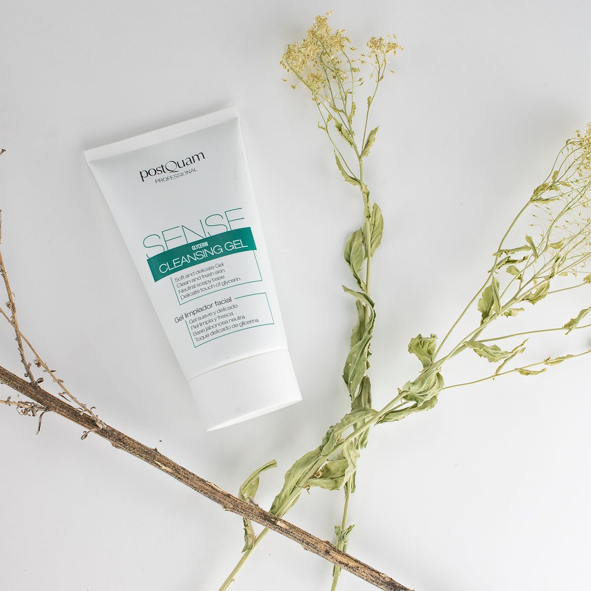 Tube blanc avec étiquette verte. Inscription : PostQuam, Sense Cleansing Gel. Sur fond blanc avec des branches.