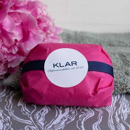 Zeep verpakt in roze papier met blauw lint en witte sticker. Opschrift: KLAR.