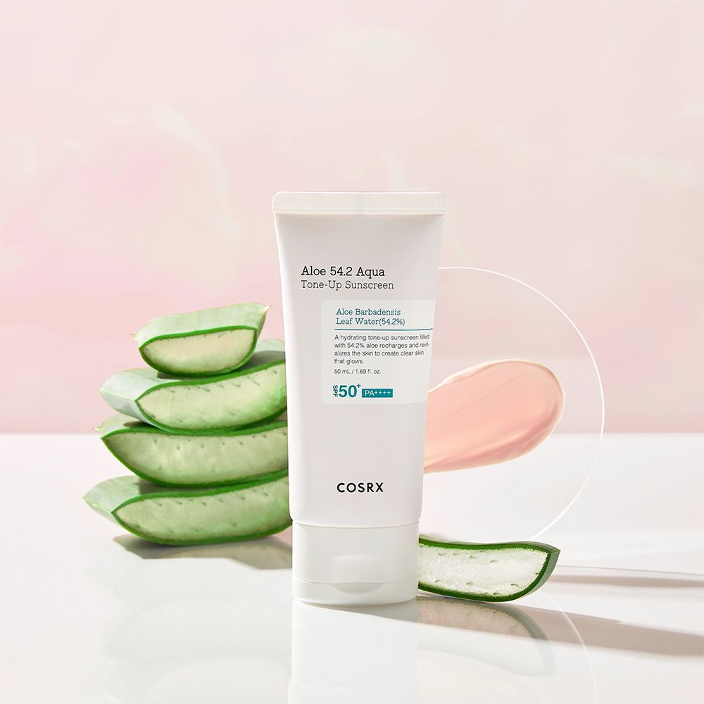 Tube de crème solaire COSRX à côté de tranches d'aloe et d'un tourbillon rose sur fond clair.