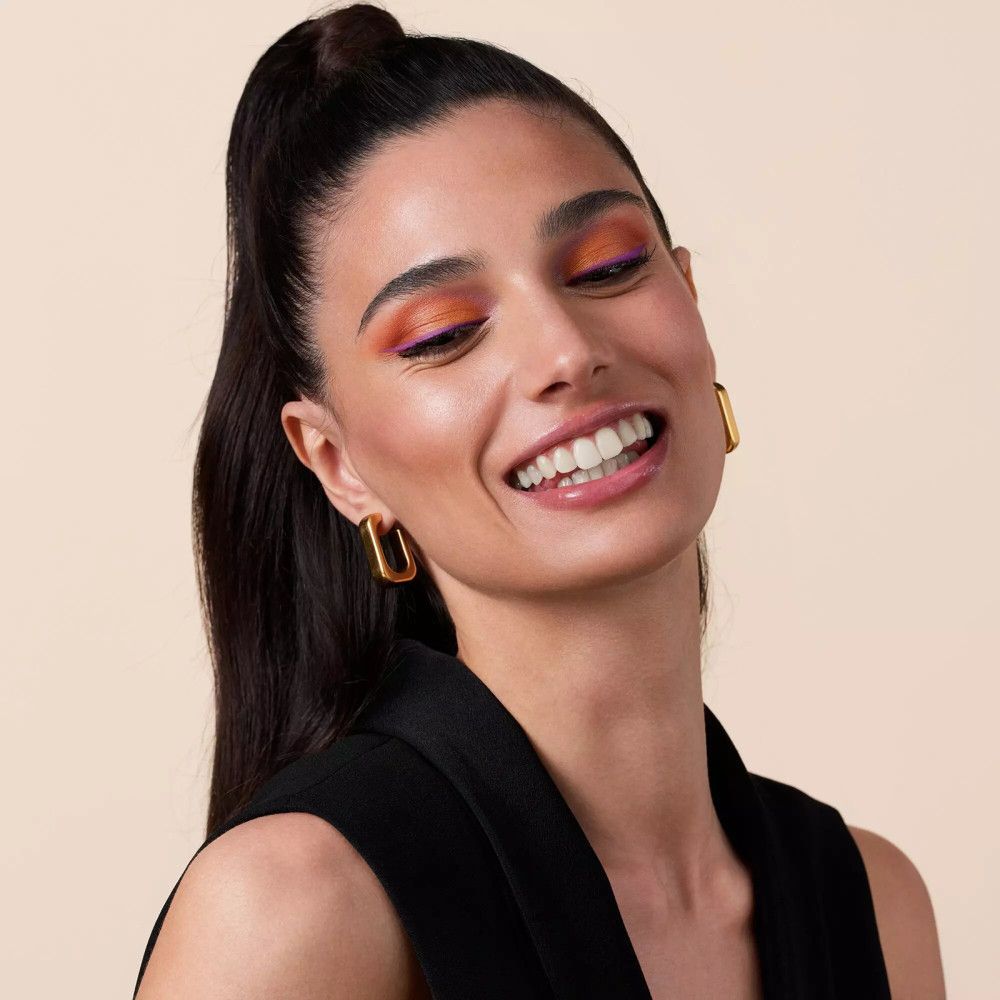 Portret van een vrouw met make-up. Ze draagt gouden oorbellen en lacht.