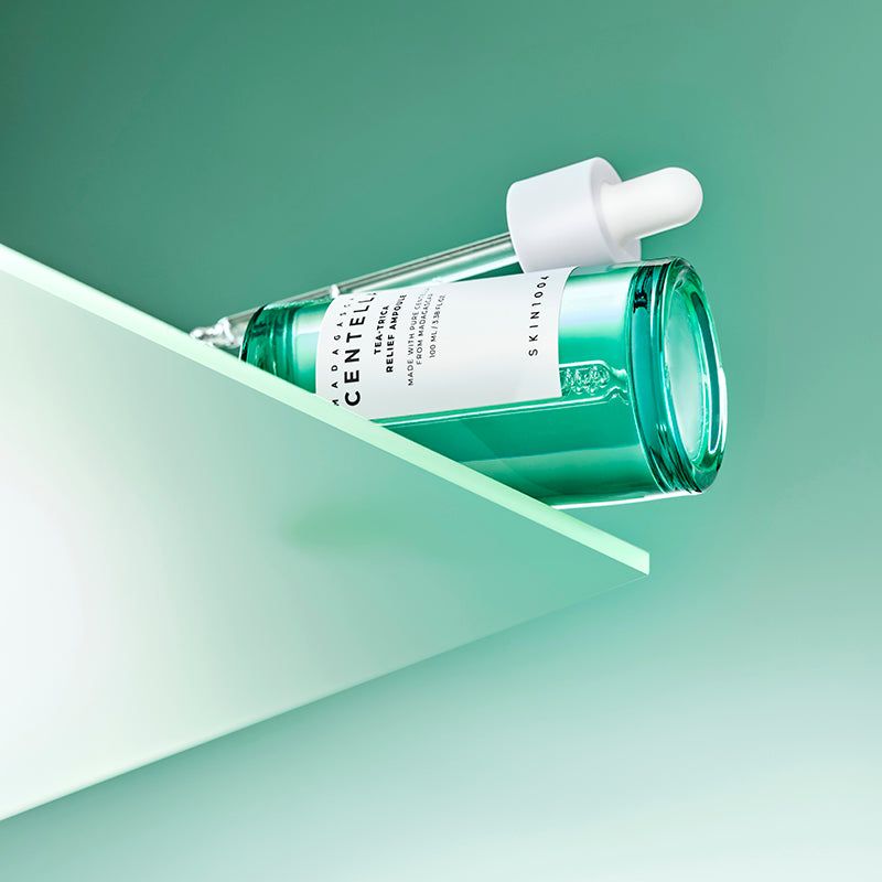 Flacon en verre vert avec bouchon et pipette blancs sur une surface blanche. Étiquette visible. SKIN1004.