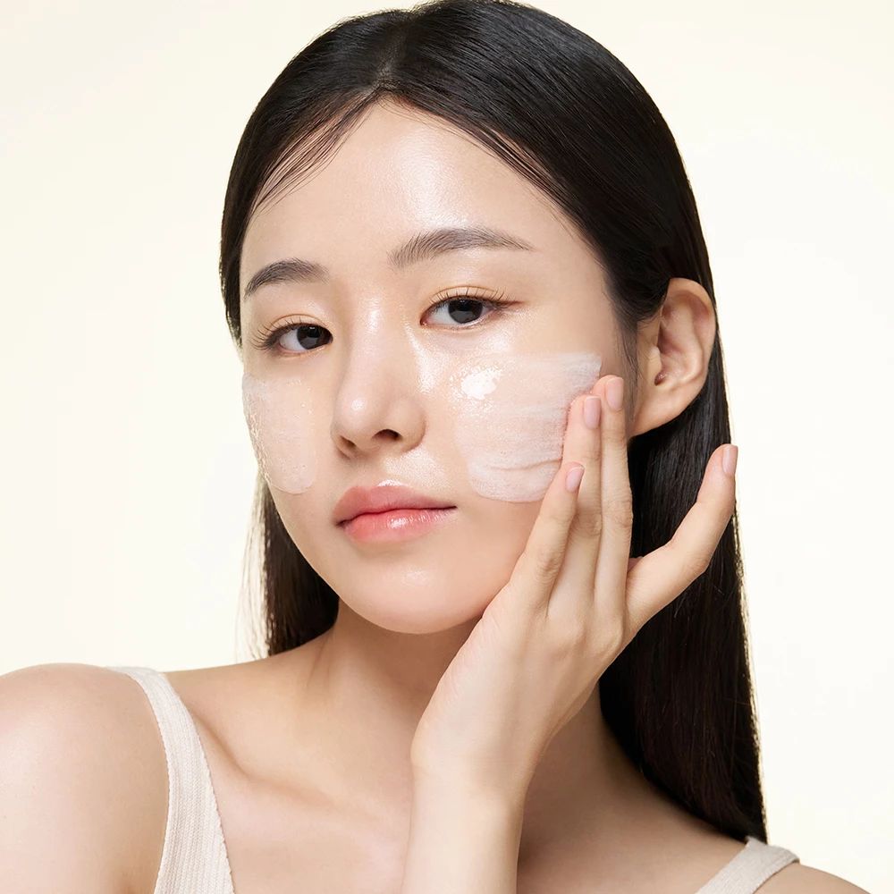 Visage d'une femme avec une substance blanche appliquée. Peau claire, cheveux foncés. Substance sur les joues et le front.