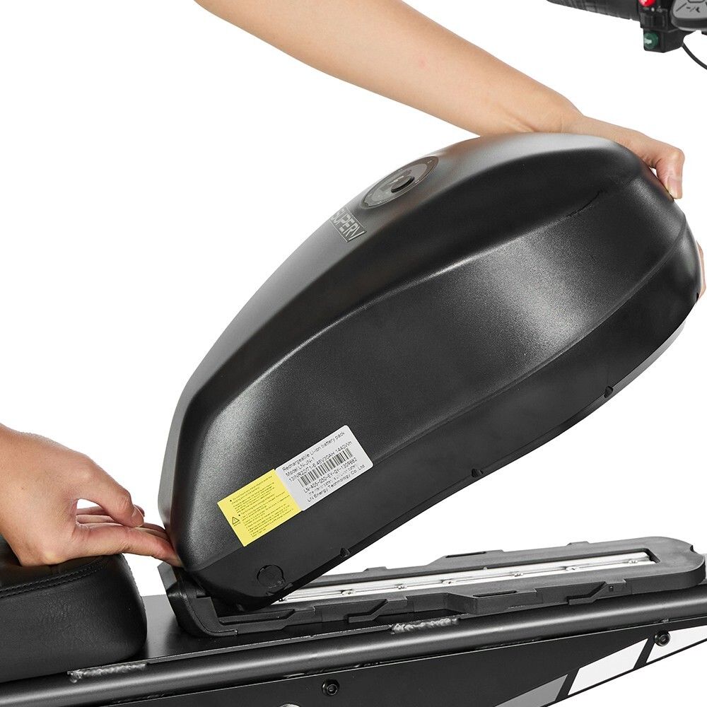 Personne plaçant une batterie noire sur le dirt bike. Cadre noir, batterie avec autocollants. Mains dans l'image.