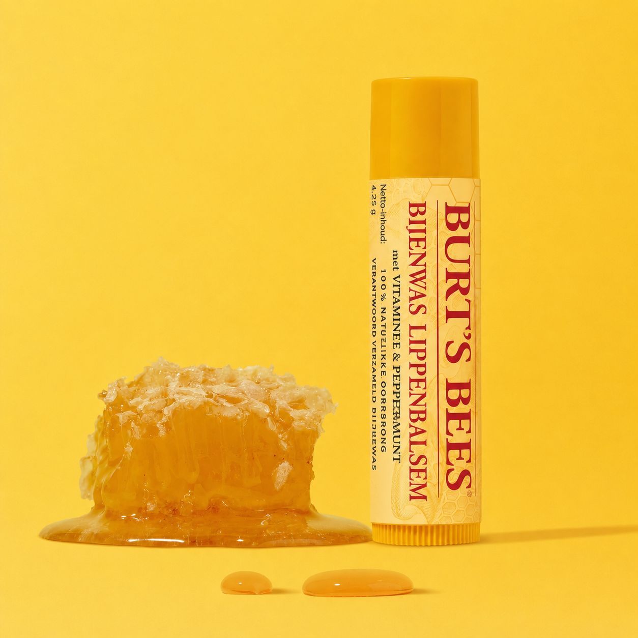 Burt's Bees lippenbalsem met honing en pepermunt. Gele verpakking, naast een stuk honingraat.