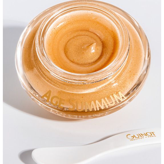 Pot en verre ouvert contenant un produit doré. Inscription AGE SUMMUM. Une spatule blanche avec le logo Guinot est à côté.