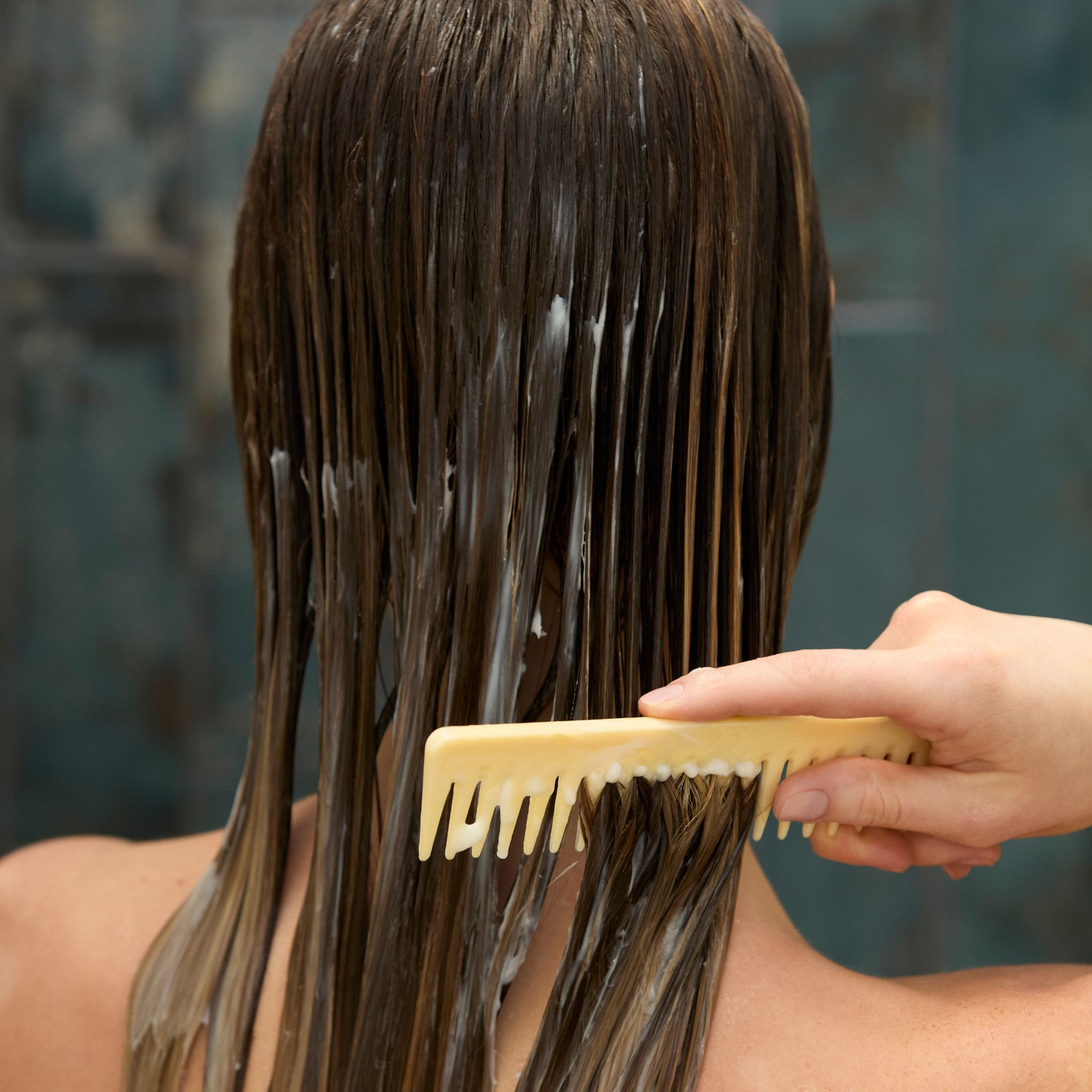 Vue arrière d'une femme peignant du revitalisant dans ses cheveux mouillés.