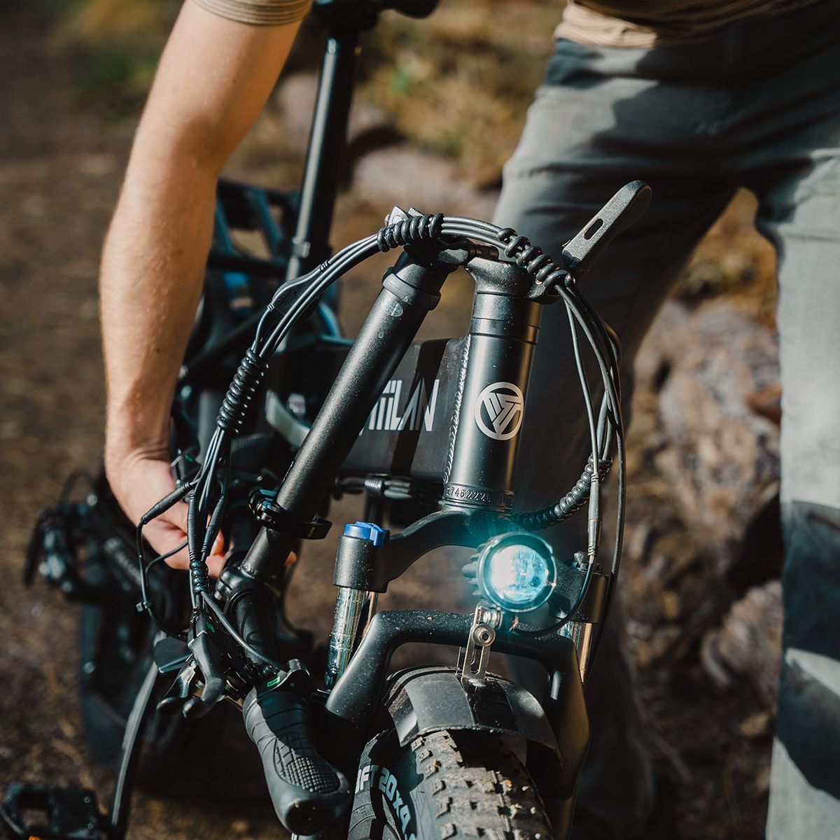 Gros plan du guidon d'un vélo électrique Vitilan V3 2.0. Phare, logo et détails visibles. Personne tenant le vélo.