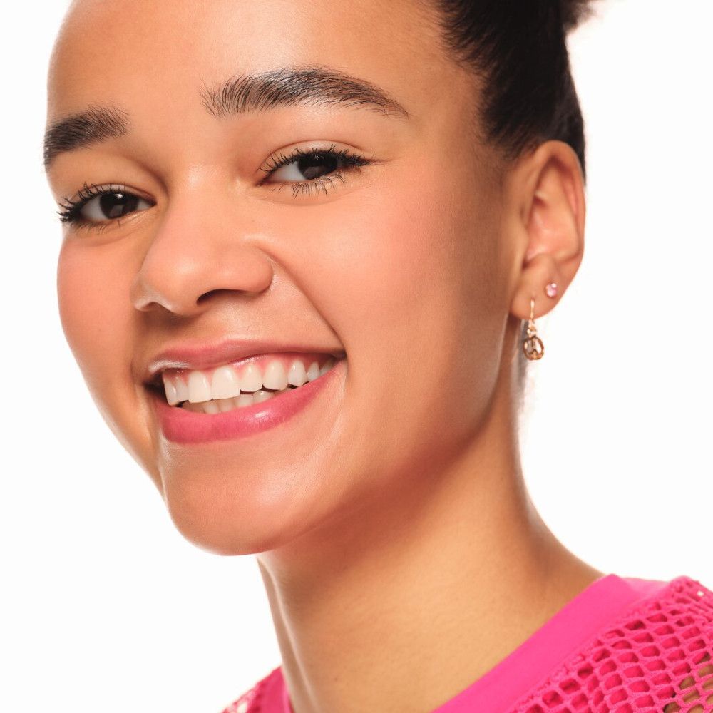 Jeune femme aux cheveux foncés et au blush rose sur les joues. Elle sourit et porte un haut rose.