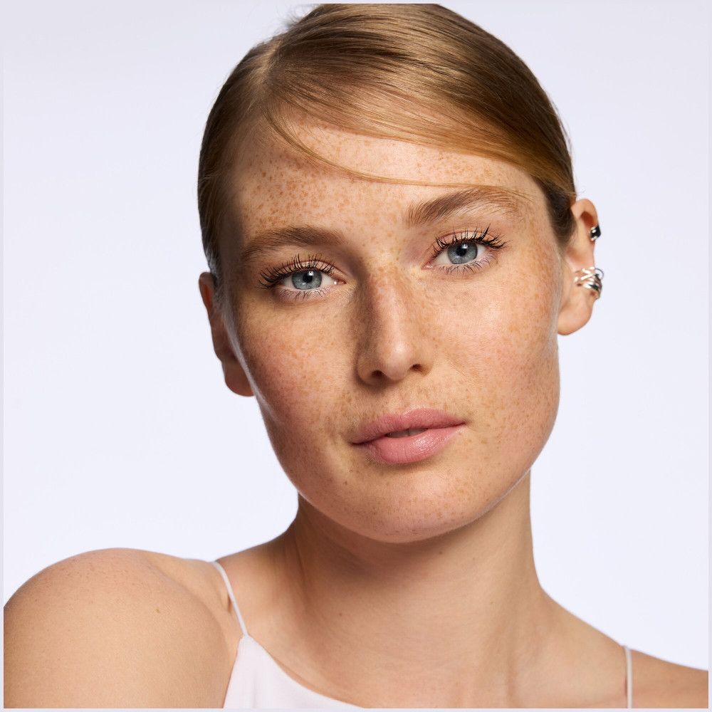 Portrait d'une femme. La femme a la peau claire, des taches de rousseur et des yeux bleus. Ses lèvres sont recouvertes de baume à lèvres.