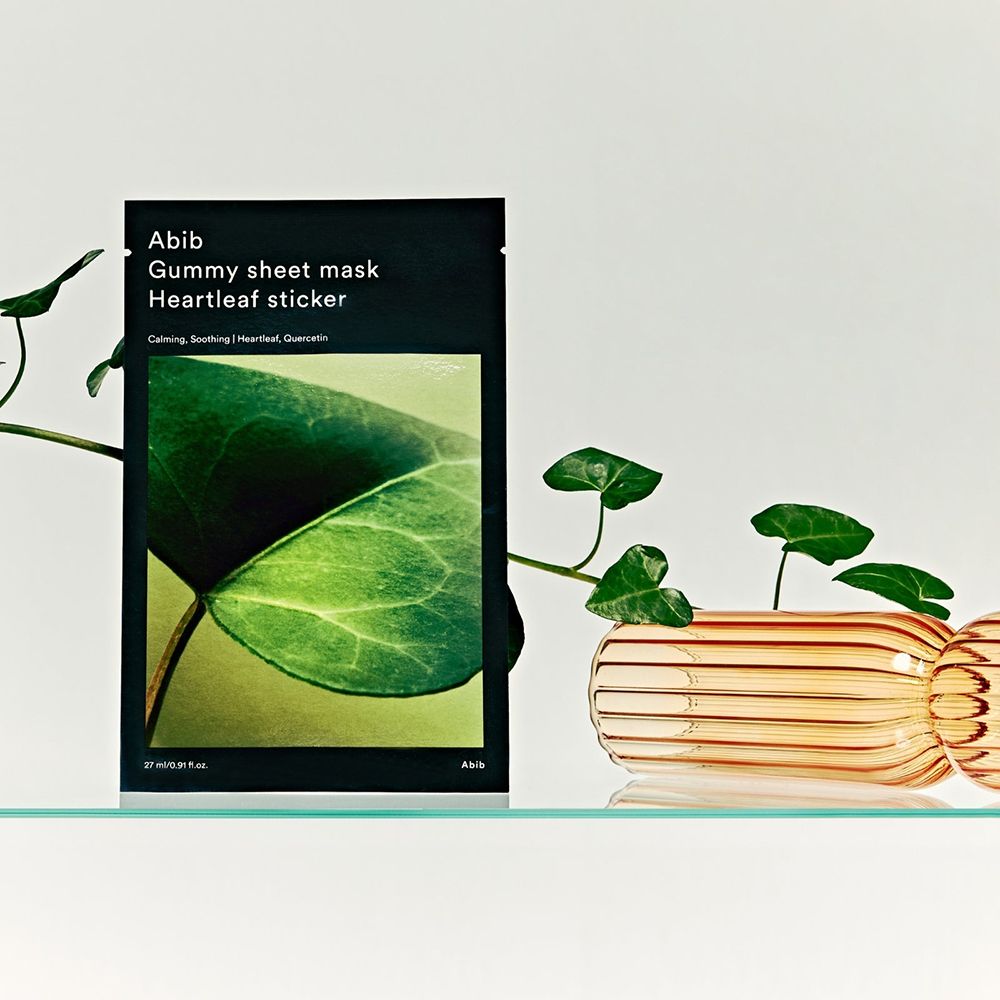 Productverpakking met bladmotief en tekst: ABIB Gummy Sheet Mask Heartleaf sticker. Decoratie met planten en glas.