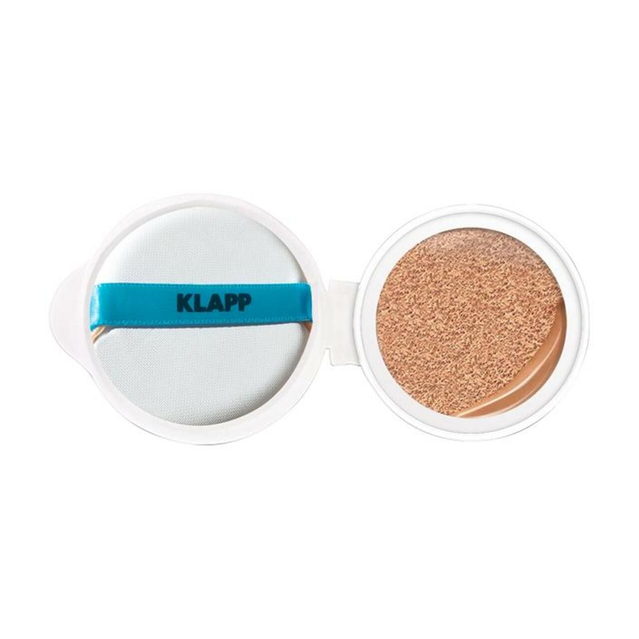 Wit cosmetica-etui met spons en getint product. De tekst "KLAPP" is zichtbaar op de band.