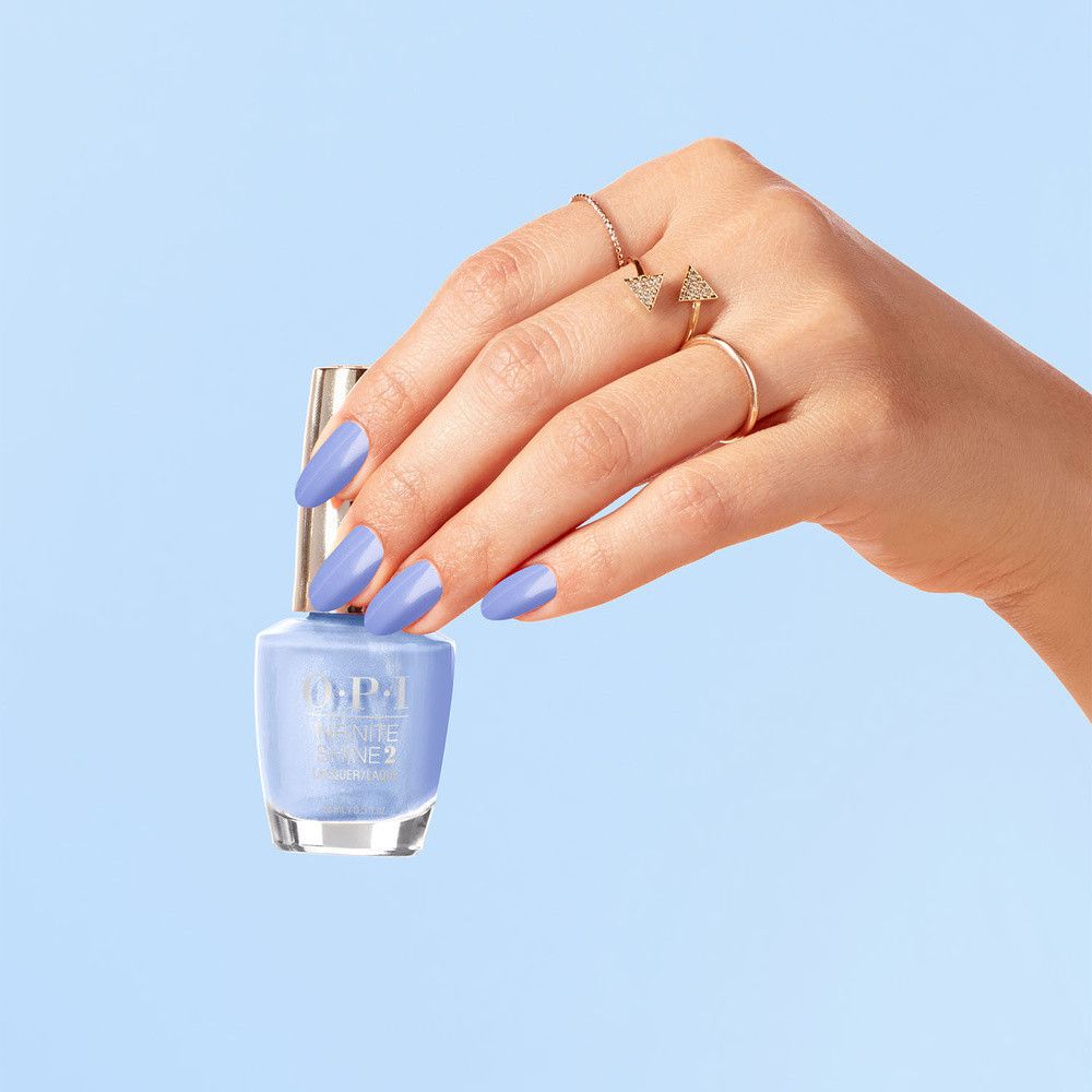 Main tenant un flacon de vernis à ongles et ongles peints en bleu clair. Fond bleu.