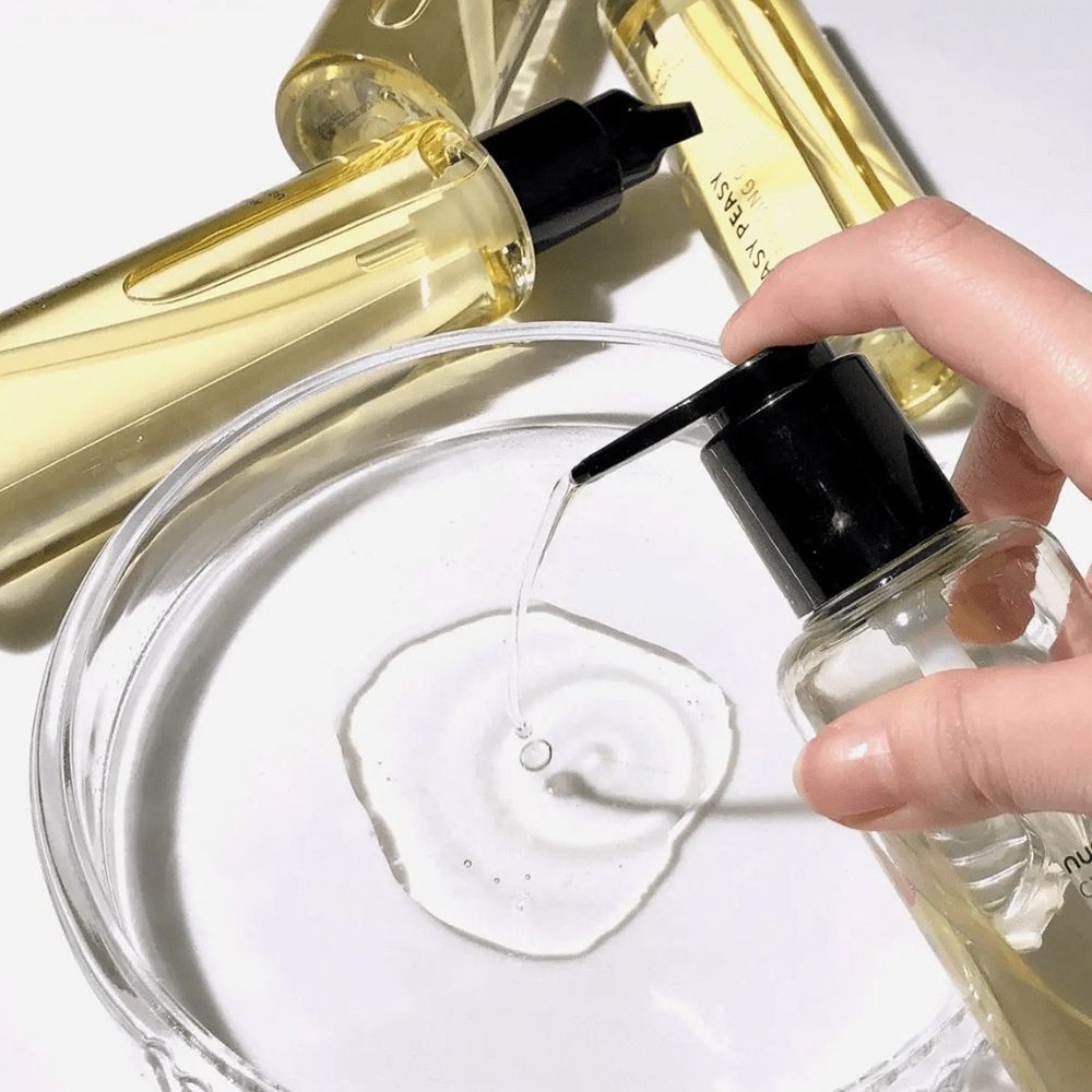 Hand bedient pomp. Olie wordt in een glazen kom gedoseerd. Meerdere flessen op de achtergrond.