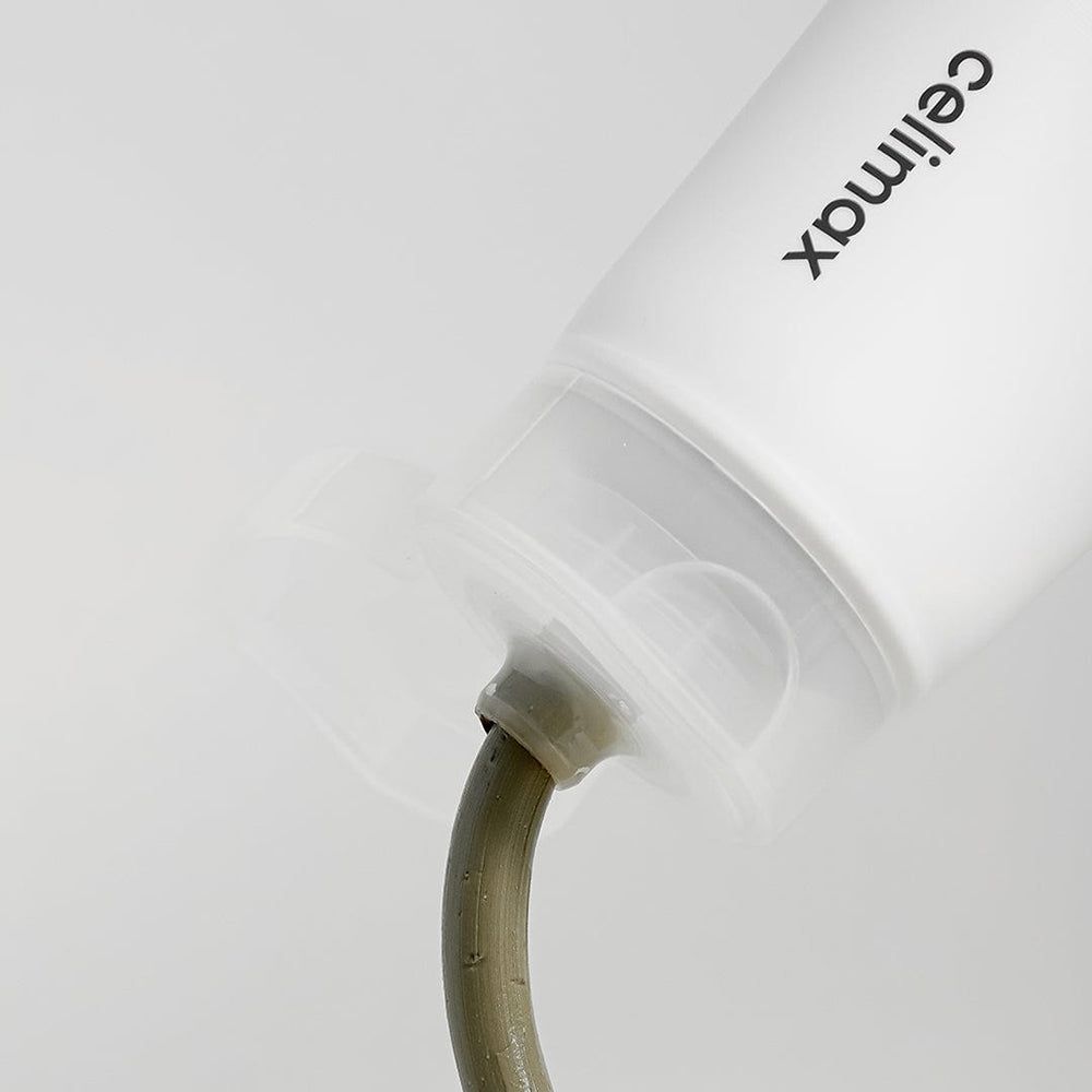 Gros plan de l'ouverture d'un tube, d'où sort un masque à l'argile gris-vert.