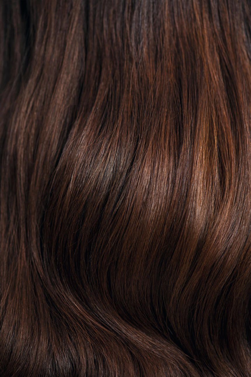 Gros plan sur des cheveux bruns ondulés. Les mèches sont colorées dans différentes nuances de brun.