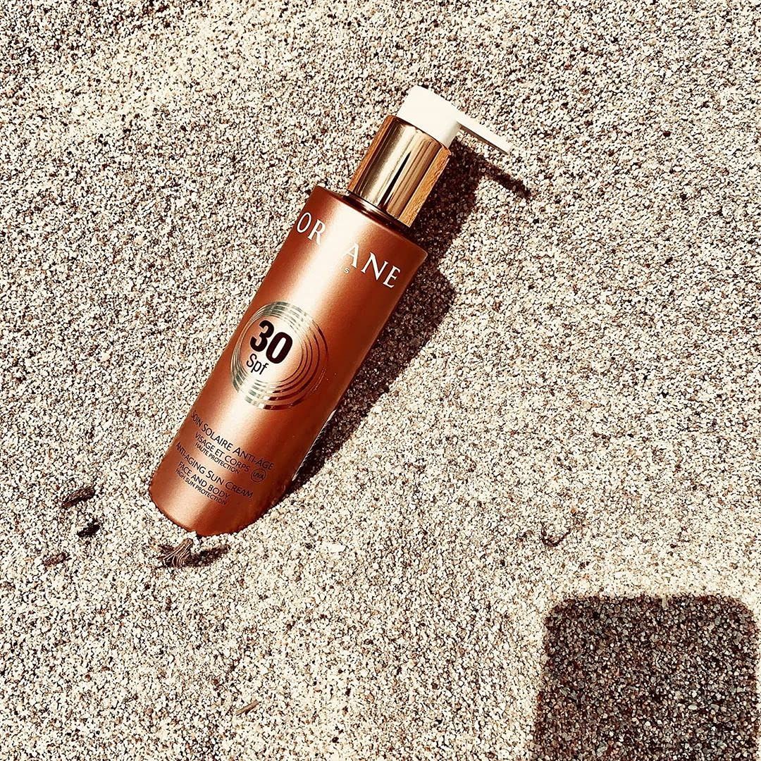 Flacon de crème solaire brun 30 SPF. Pompe dorée. Sur du sable. Marque Orlane.