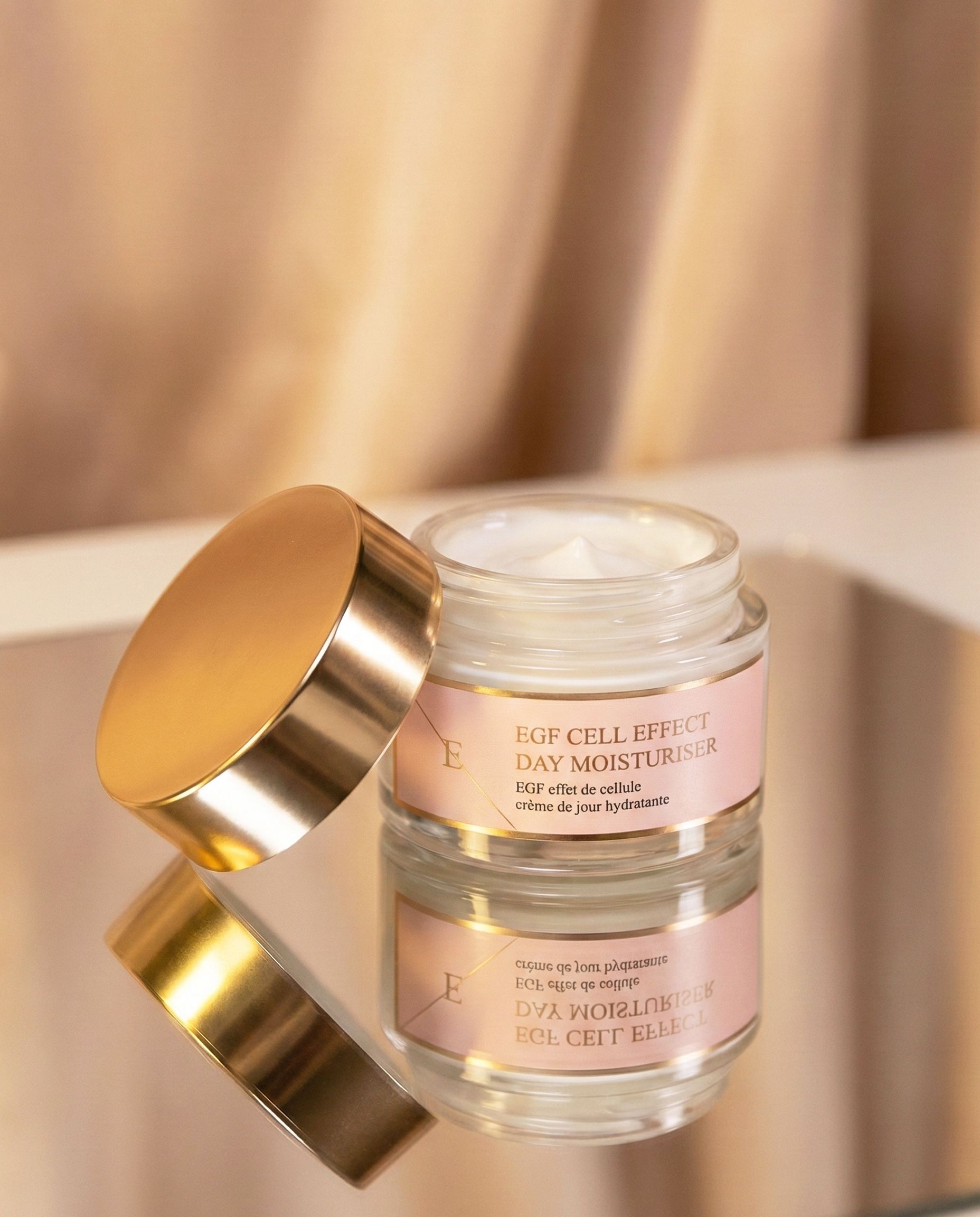 Pot de crème en verre ouvert avec couvercle doré, rempli de crème blanche, sur miroir.