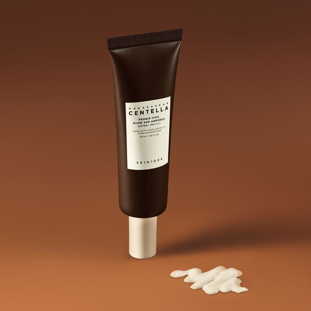 Tube marron avec étiquette blanche. Nom du produit et marque visibles. À côté, une goutte de crème. Sur fond marron.
