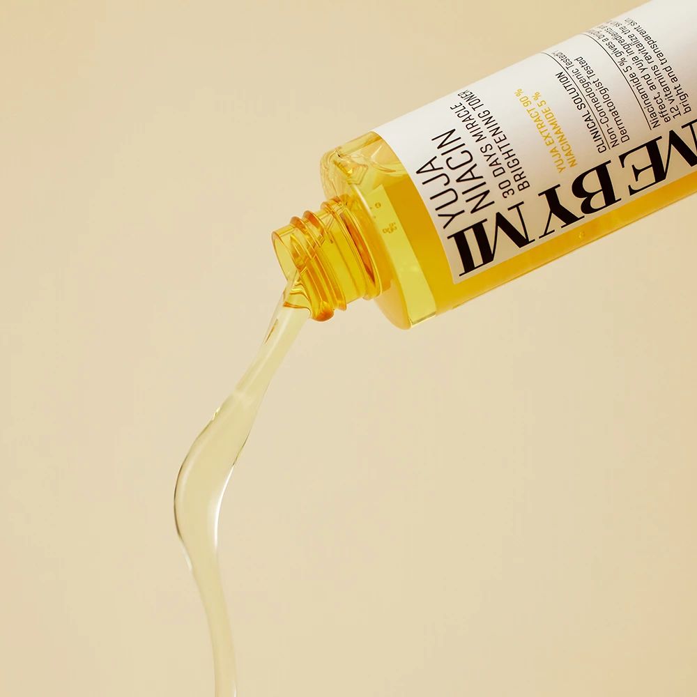 Liquide jaune coulant d'un flacon avec une étiquette blanche. Texte : Yuja Niacin, 30 Days Miracle Brightening Toner.