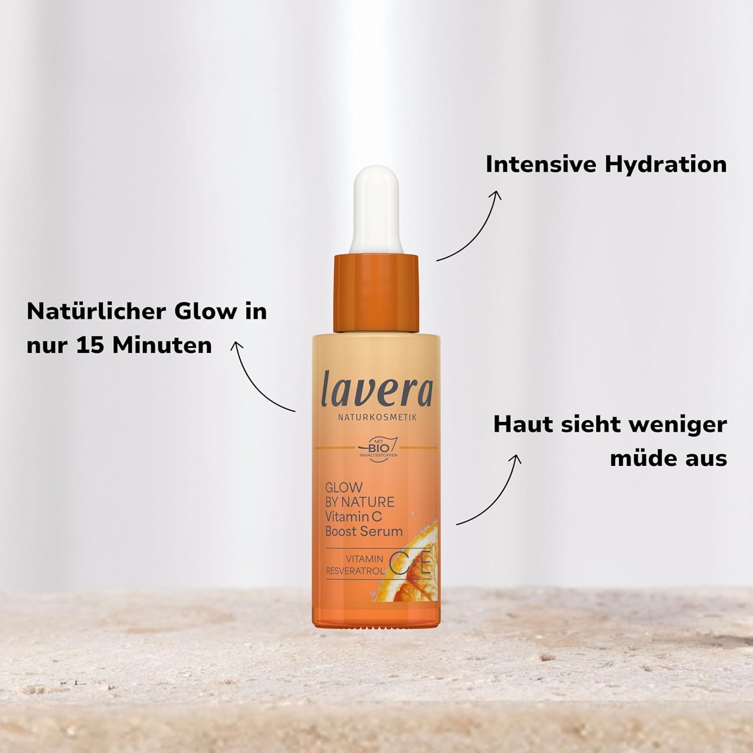 Flacon de sérum avec texte. Flacon avec bouchon orange. Texte: lavera, Glow By Nature Vitamin C Boost Serum. Flèches pointant vers le texte.