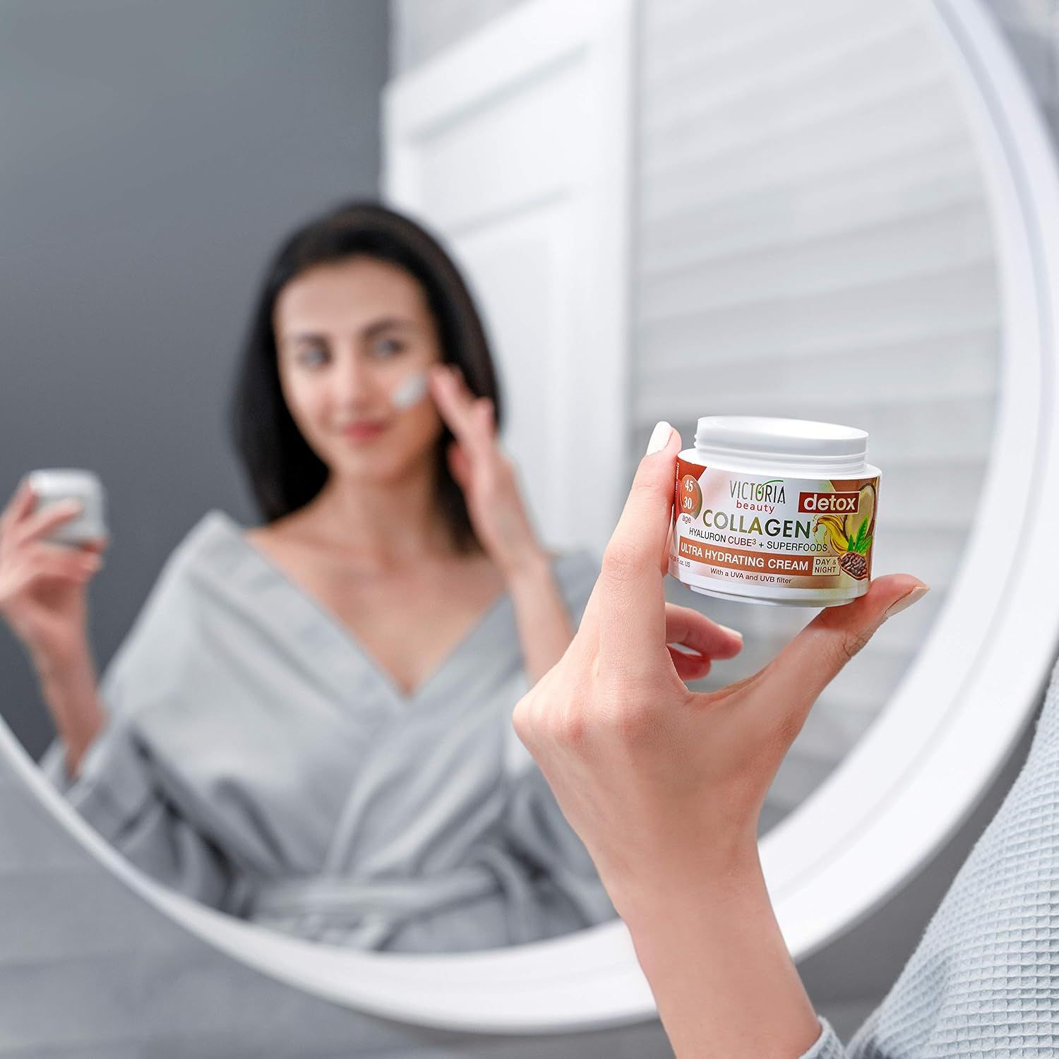Een vrouw brengt Victoria Beauty Collageencrème aan, houdt de pot in de spiegel.