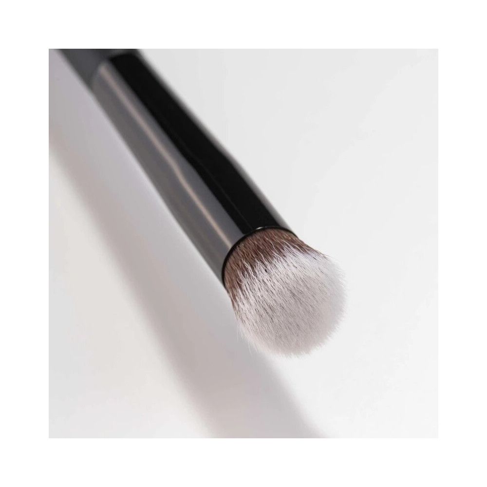 Pinceau avec manche noir et tête de pinceau claire. Vue rapprochée, diagonale.