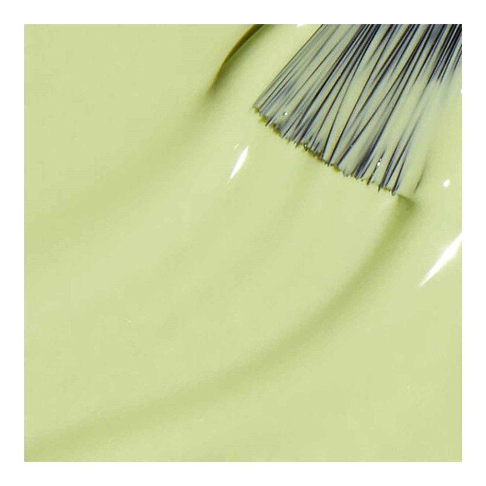 Nagellak applicator op lichtgroen lak oppervlak. Borstelharen van de kwast zijn zichtbaar.