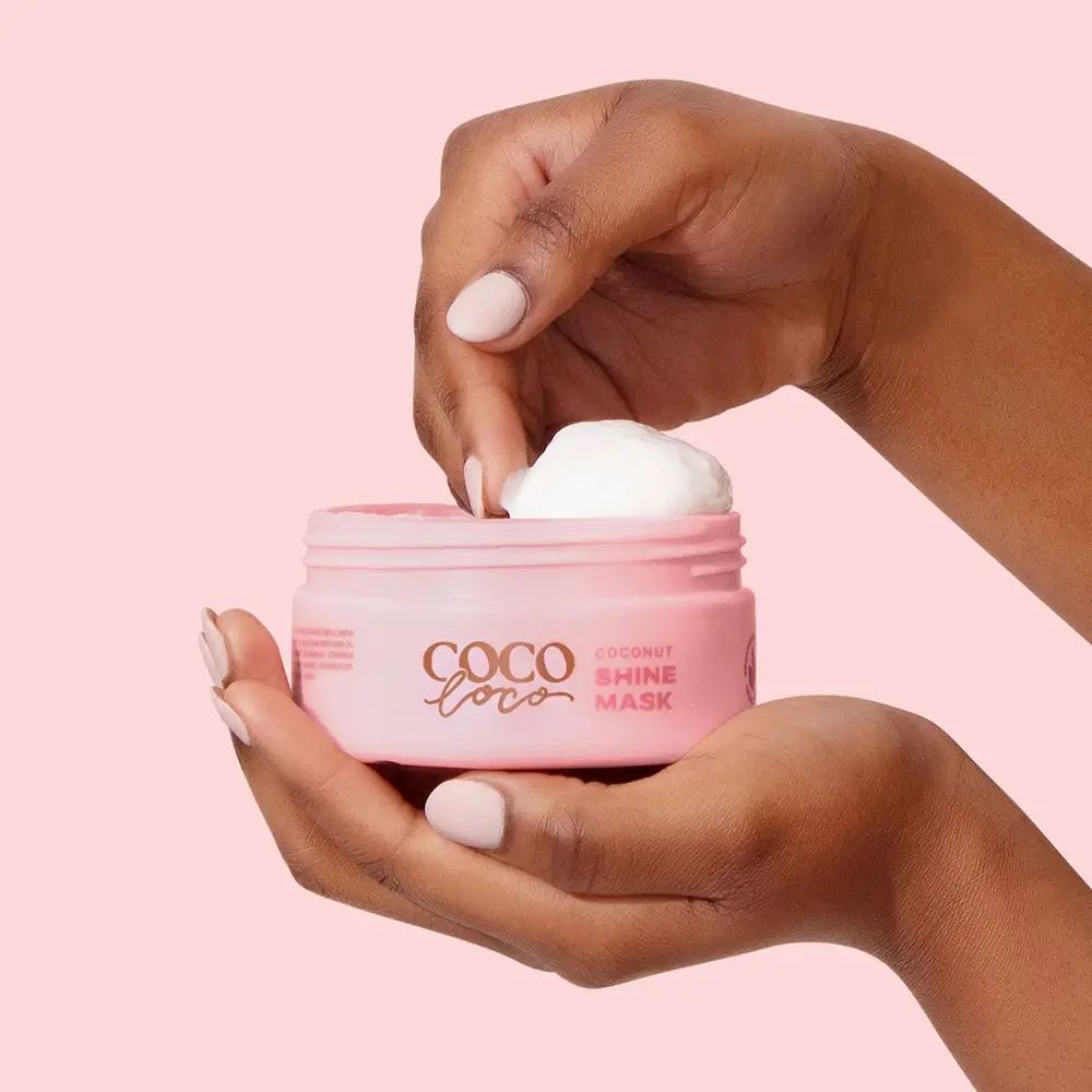 Handen houden een open roze pot Coco Loco, Coconut Shine Mask, met crème.