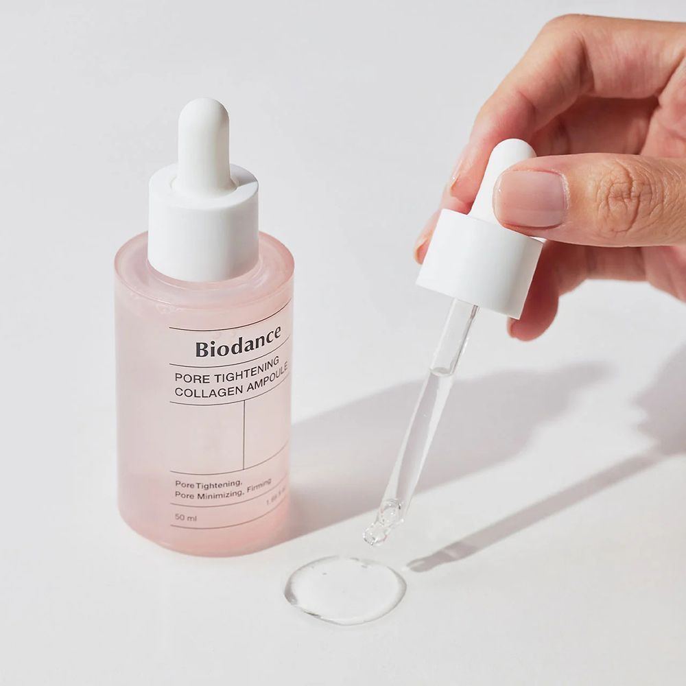 Hand houdt een roze fles met witte dop. Opschrift: Biodance Pore Tightening Collagen Ampoule. Druppels.