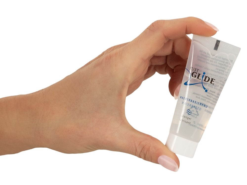 Main tenant un tube. Inscription: JUST GLIDE, Wasserbasiert, Medizin. Gleitgel. Fermeture blanche.