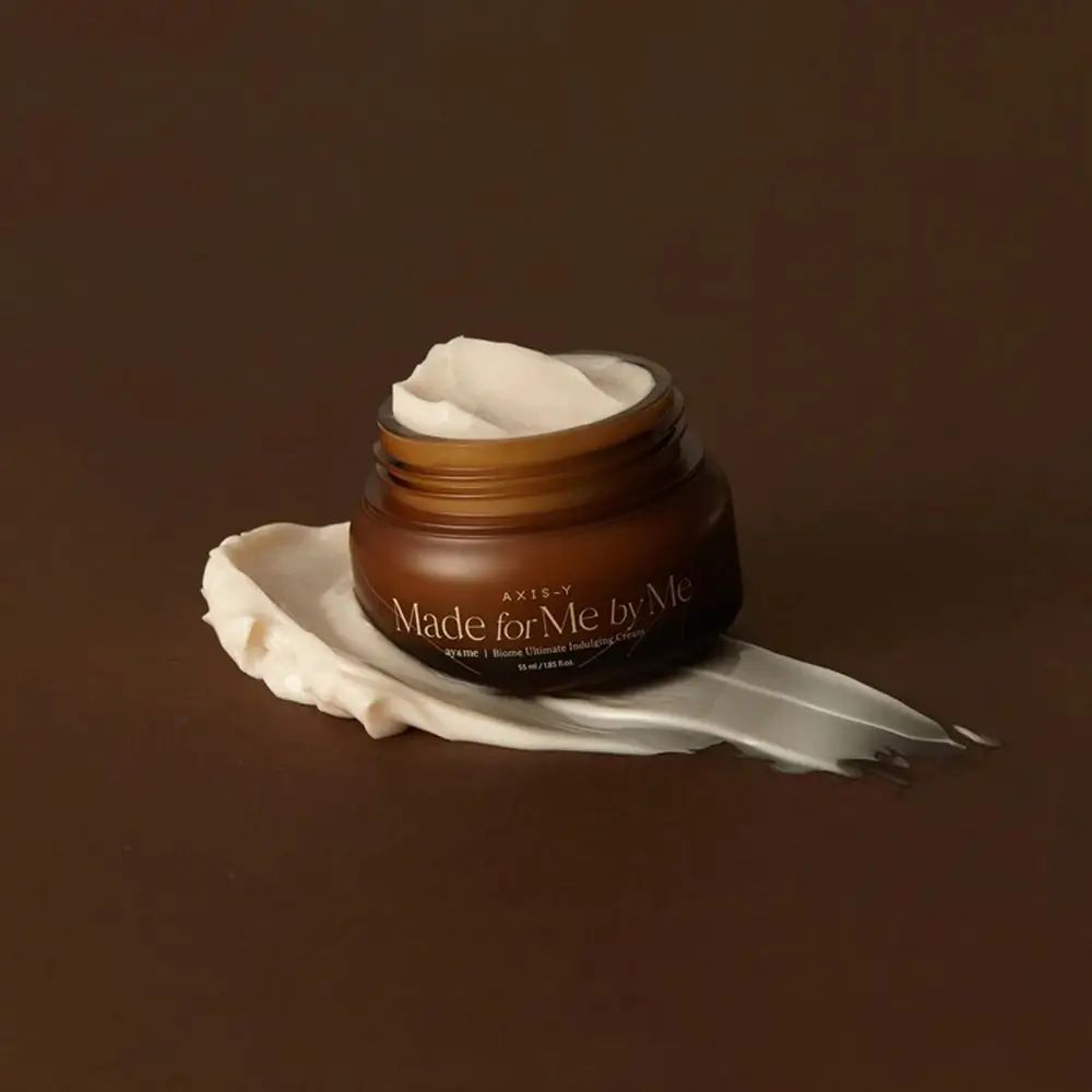 Pot de crème marron avec crème sur une trace. Inscription : AXIS-Y, Made for Me by Me, Biome Ultimate Indulging Cream.