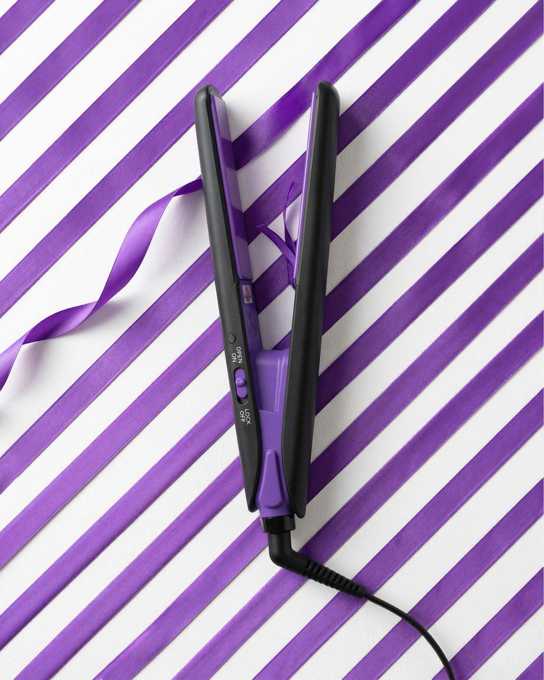 Mini-lisseur noir et violet. Plaques ouvertes, connexion par câble. Sur motif rayé violet et blanc.