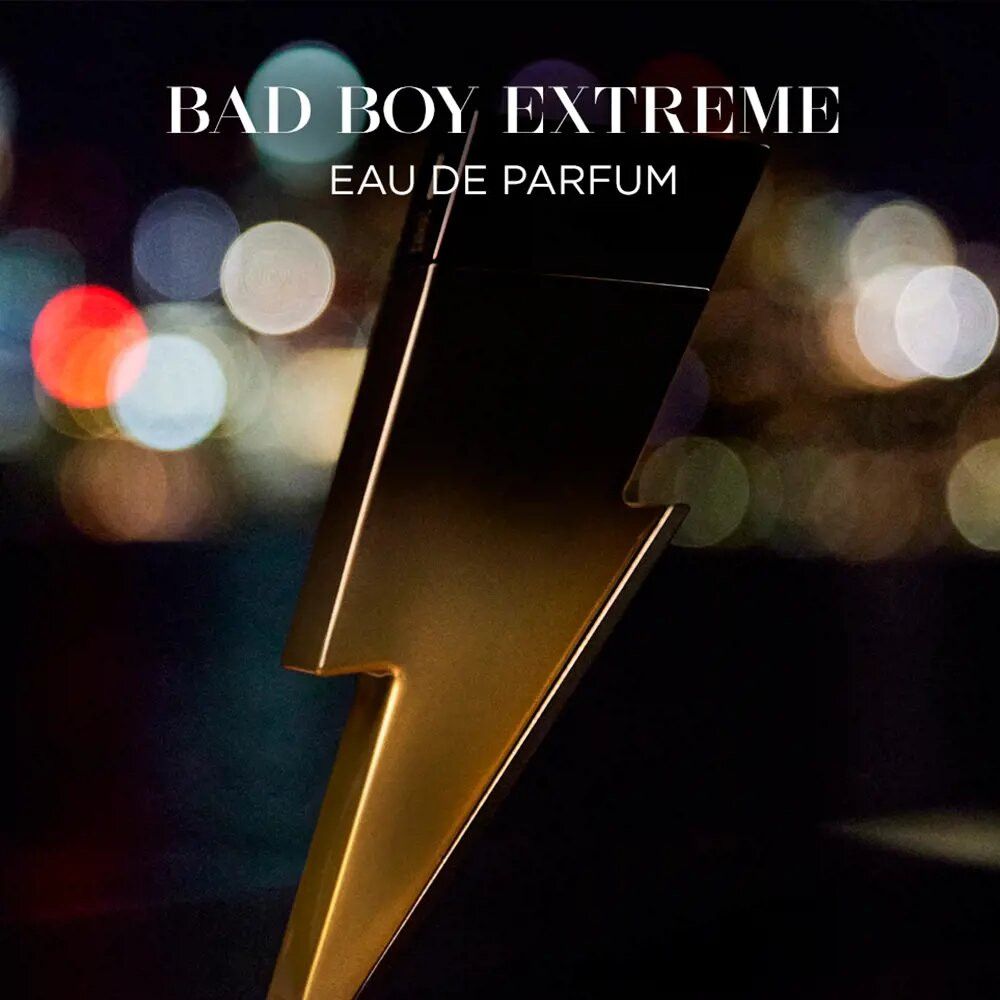 Gouden bliksemvormige parfumfles. Opschrift: Bad Boy Extreme, Eau de Parfum. Achtergrond: wazige lichten.