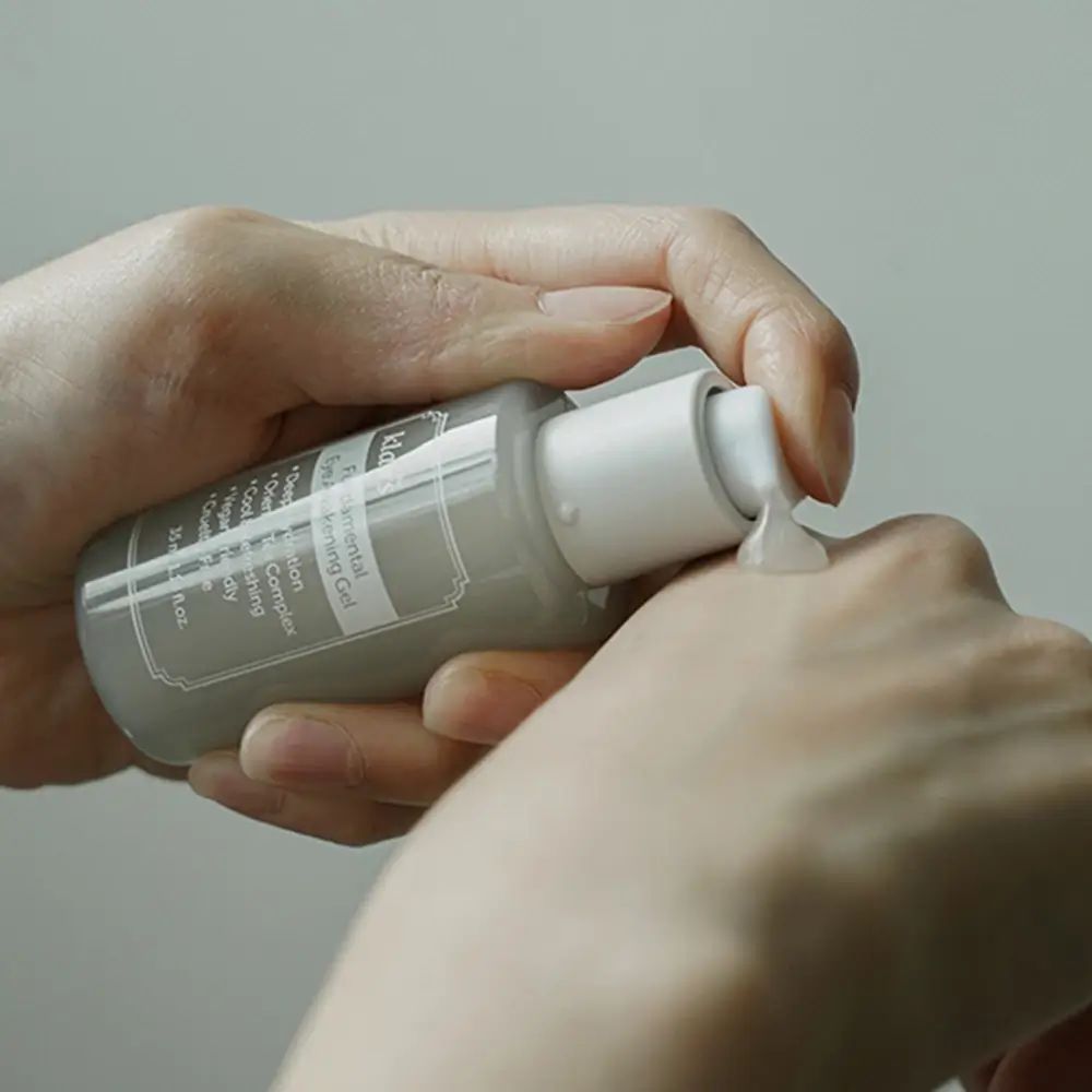 Handen die product uit pompflacon persen. Opschrift: Fundamental Eye Awakening Gel, klairs.