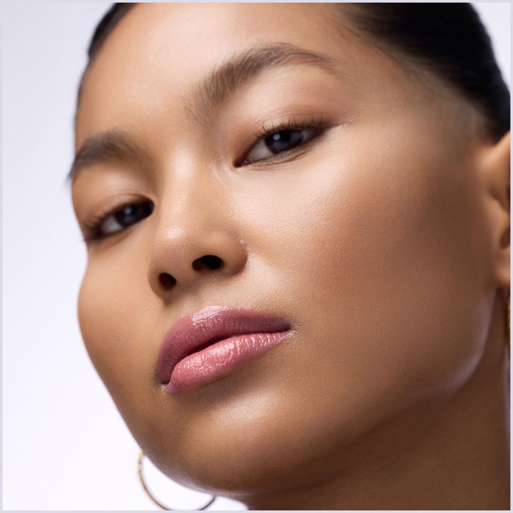 Gros plan sur un visage avec repulpeur à lèvres appliqué. Fini brillant, teinte rose. Sourcils et peau visibles.
