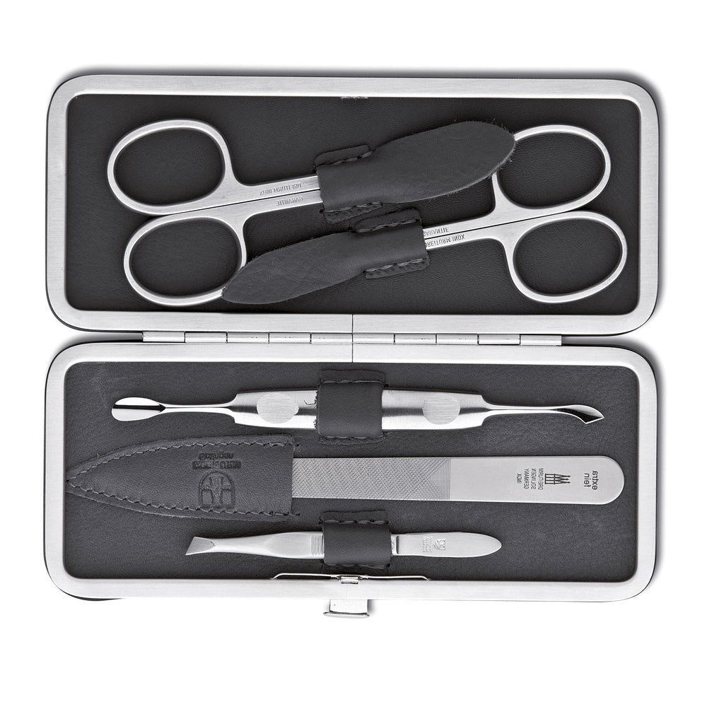 Trousse de manucure ouverte avec ciseaux, lime à ongles, repousse-cuticules et pince à épiler. Cuir noir, outils argentés.