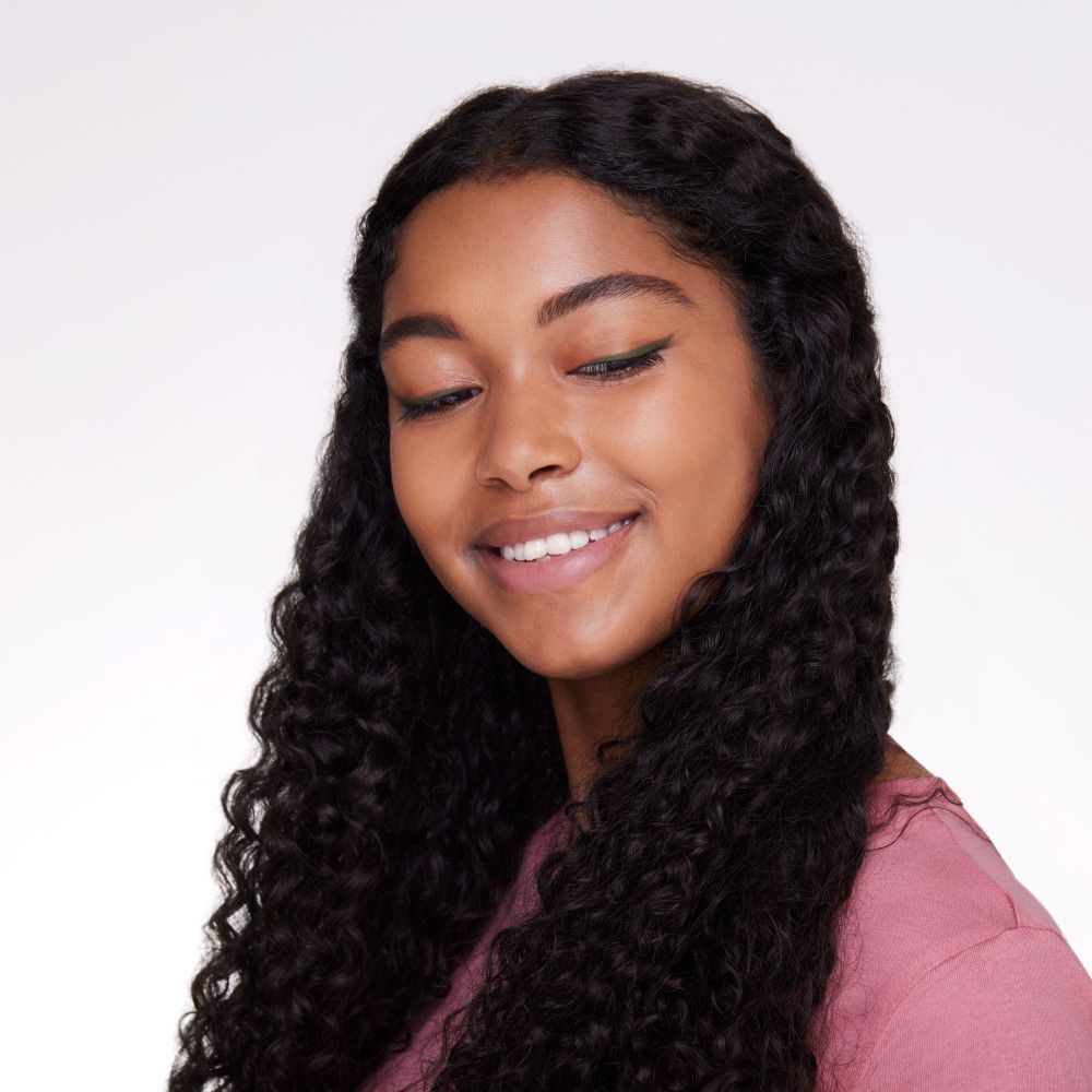 Portrait d'une femme aux longs cheveux noirs bouclés. Elle porte un trait d'eye-liner.