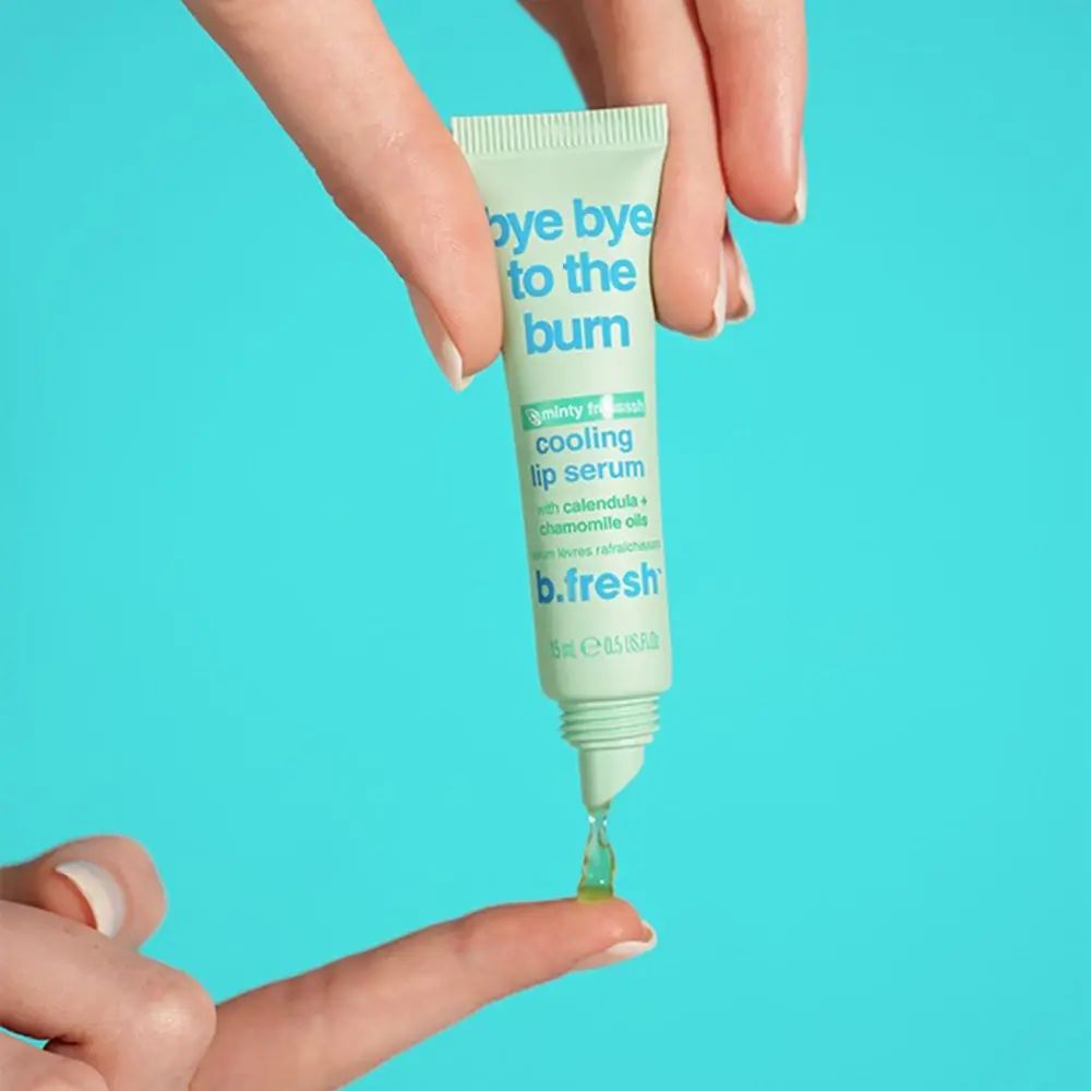 Handen houden een groene tube vast. Een druppel serum op een vinger. Opschrift: Bye Bye to the Burn, Cooling Lip Serum.