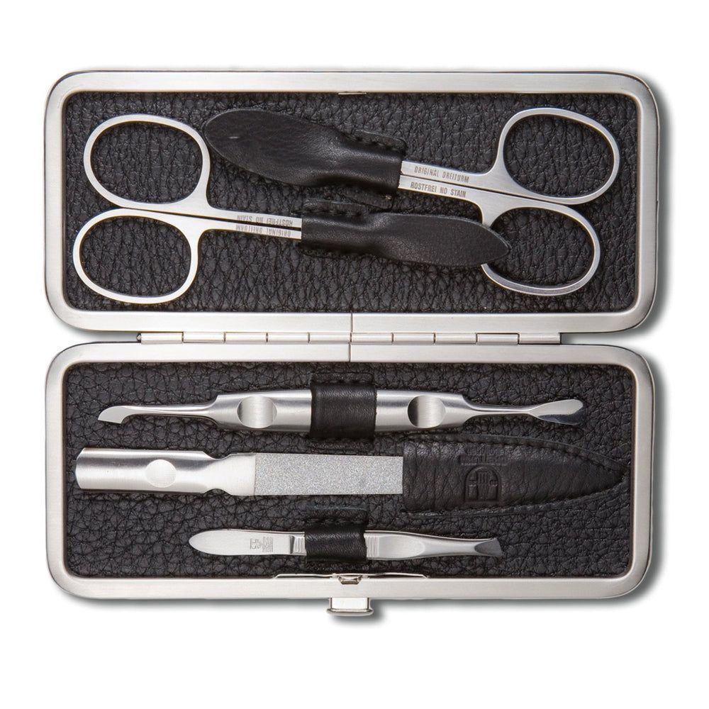 Coffret manucure noir ouvert. Ciseaux, coupe-ongles, lime, repousse-cuticules et pince à épiler. Métal et cuir.