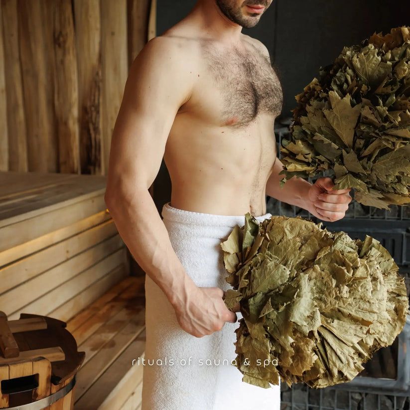 Man houdt twee bundels berkenrijshout vast. Hij draagt een handdoek. Tekst: Rituals of sauna & spa.
