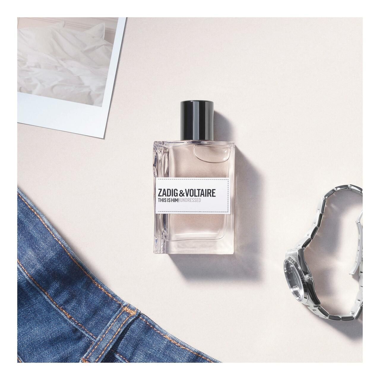 Zadig & Voltaire This is Him! Undressed EdT Nat. Spray. Fles op lichte achtergrond. Jeans en accessoires.