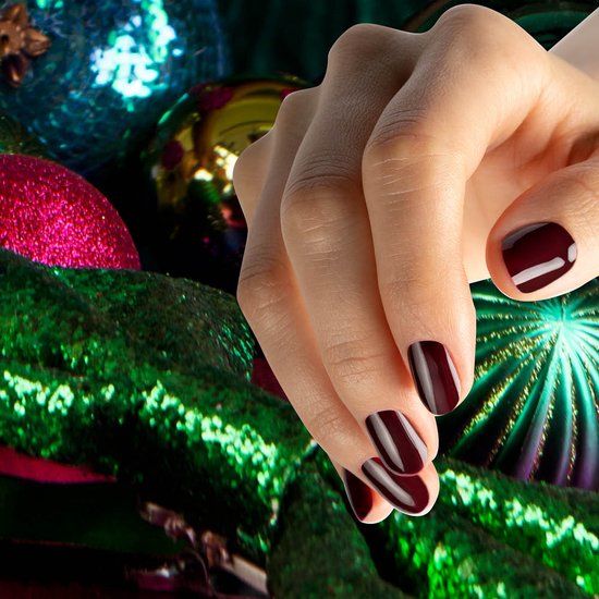 Main avec ongles vernis. Vernis à ongles Pinot Noir. Arrière-plan : décorations de Noël avec boules vertes et roses.