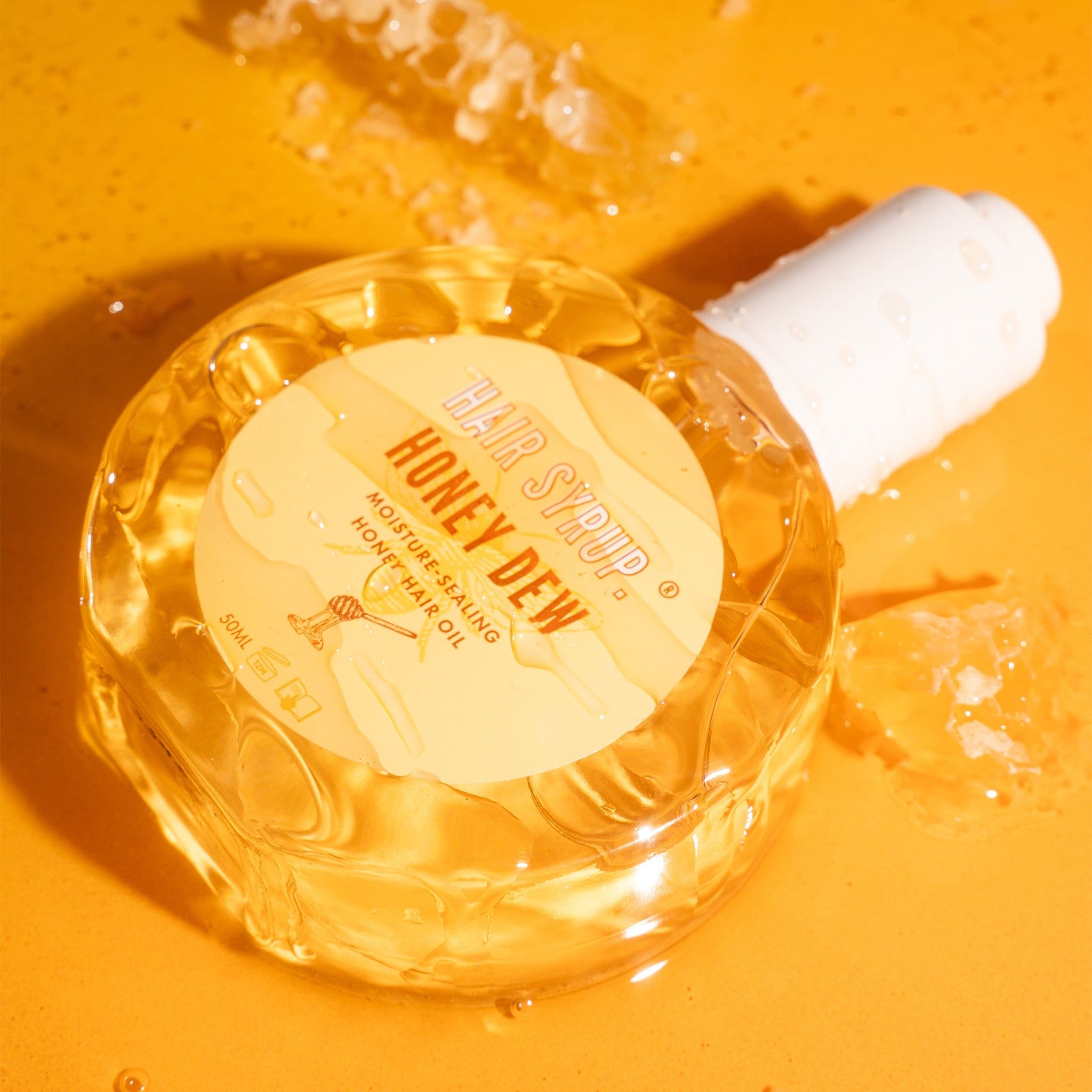 Ronde glazen fles met witte dop. Etiket met tekst. Fles ligt op gele ondergrond. Honingraten op de achtergrond.