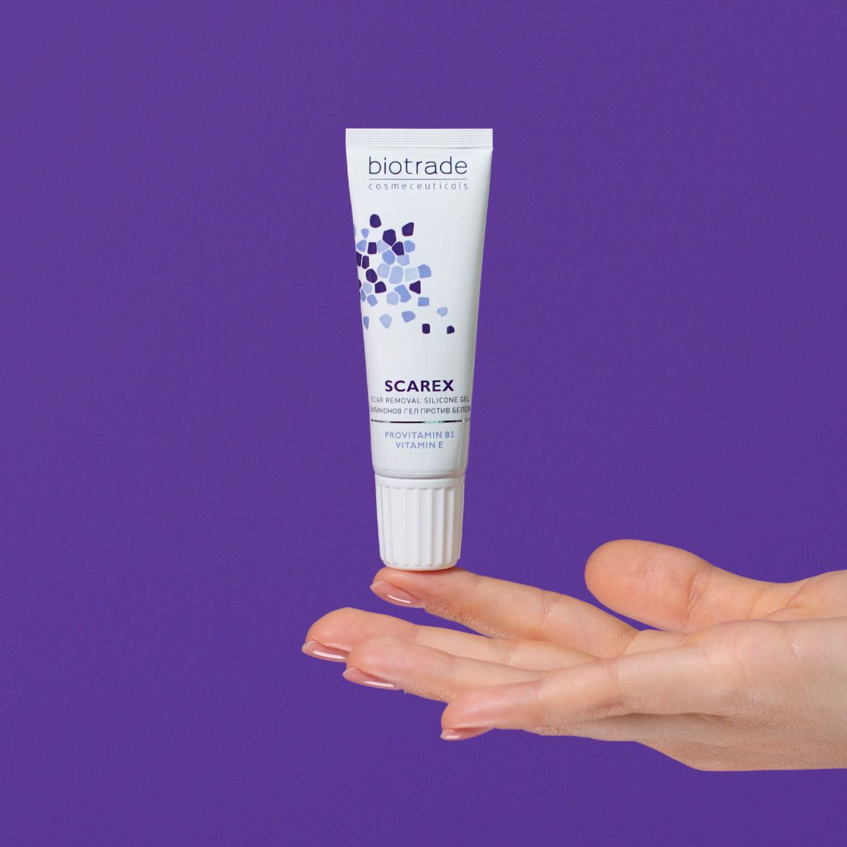 Wit-blauwe tube met productnaam en logo, vastgehouden door een hand, tegen paarse achtergrond.