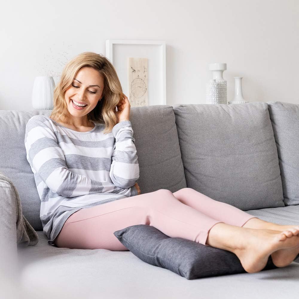 Femme assise sur un canapé avec un coussin repose-pieds gris sous ses pieds.