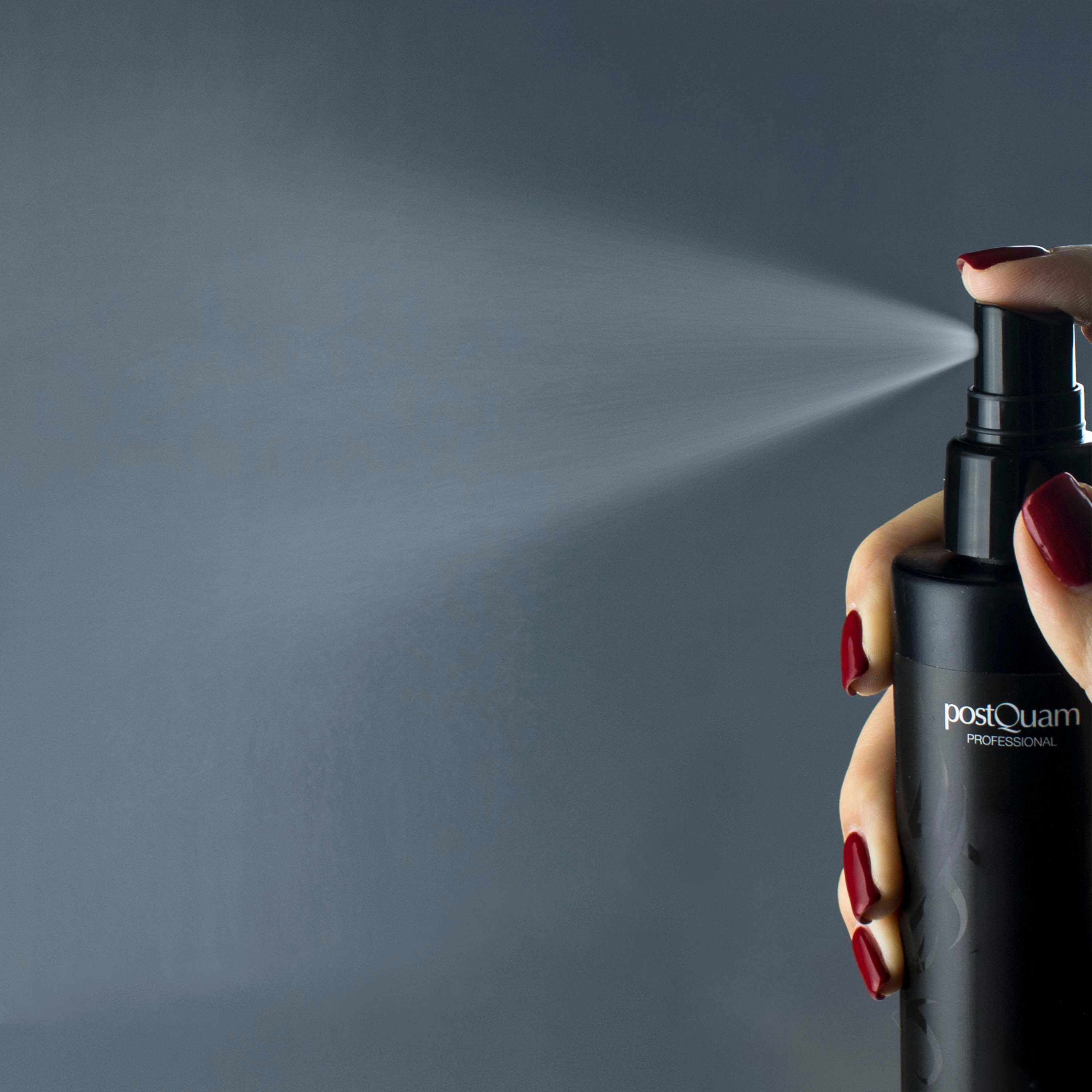 Hand met rode nagellak spuit uit een zwarte fles. Merk PostQuam is zichtbaar.
