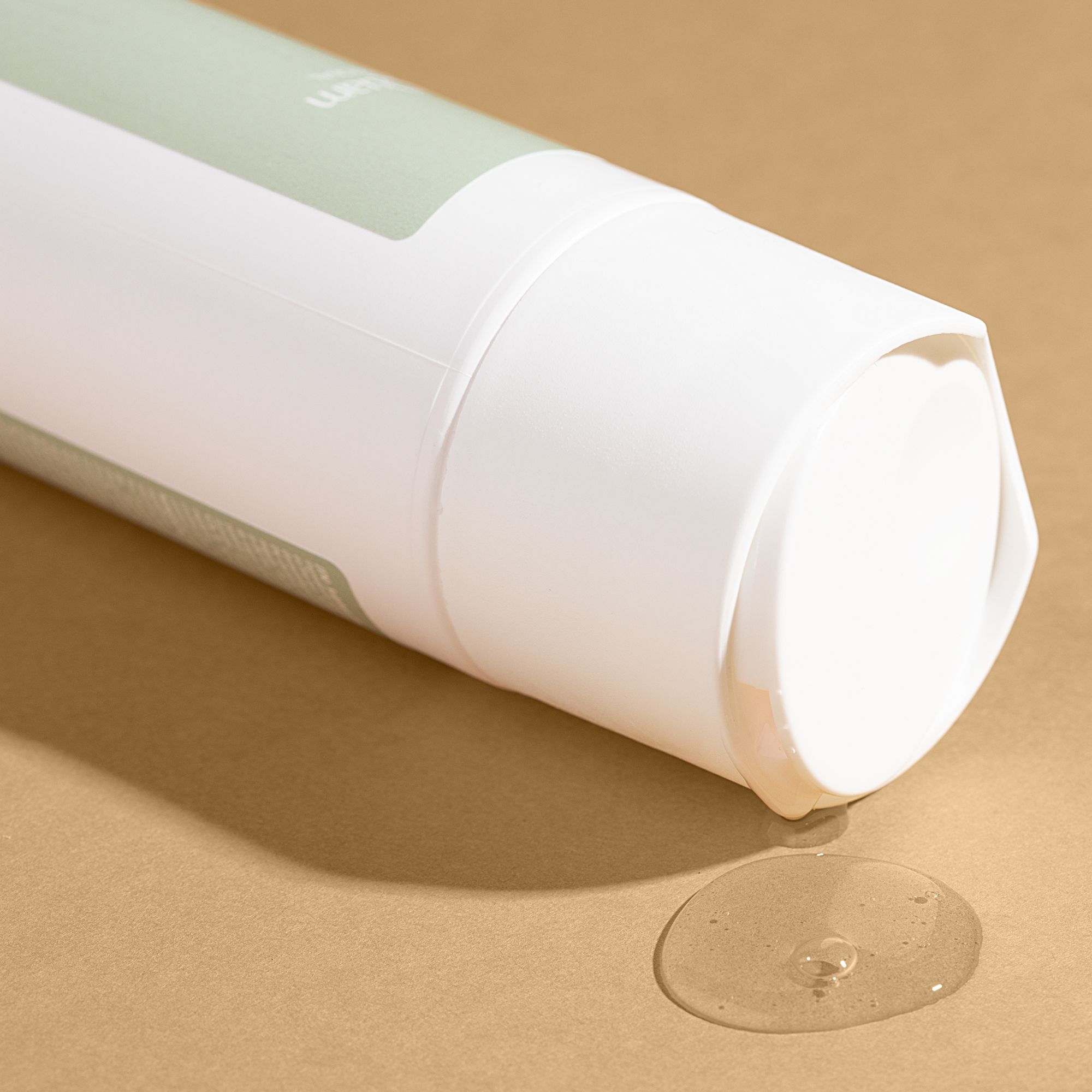 Tête de flacon de shampooing blanc avec liquide clair qui coule sur fond brun.