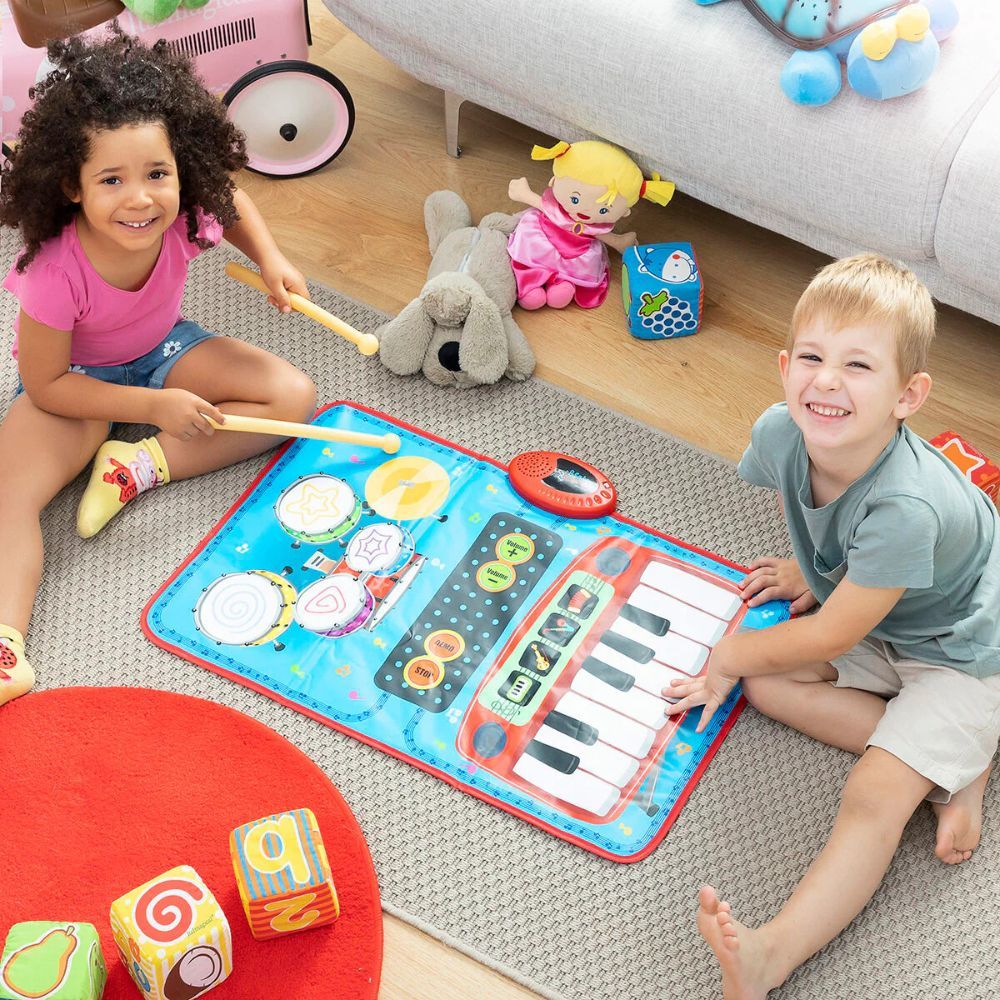 Enfants jouant sur un tapis musical bleu avec tambours et touches de piano. Les enfants tiennent des baguettes. Jouets et coussins en arrière-plan.